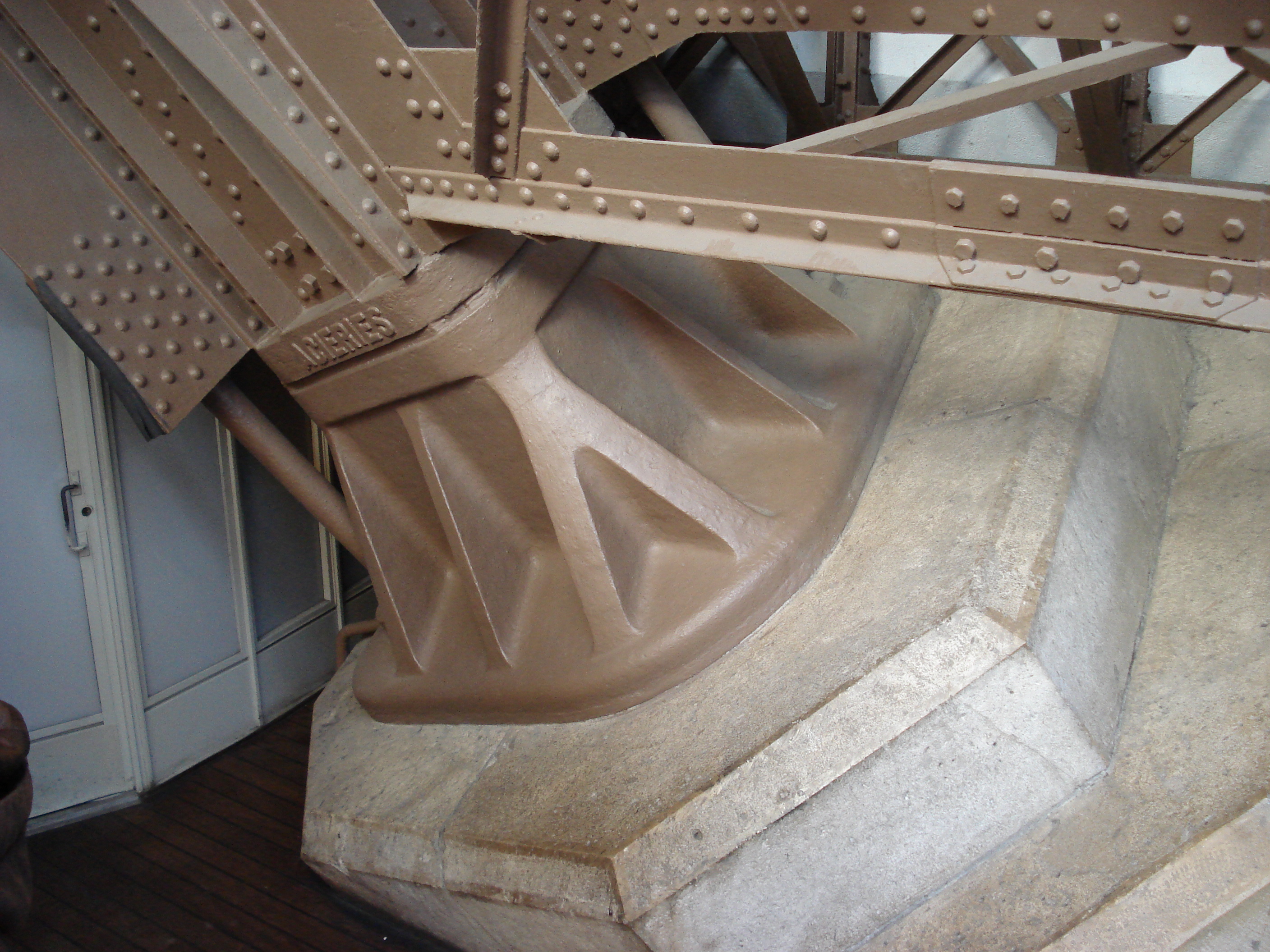 Close structural view of the Eiffel Tower ironwork meeting the limestone and masonry base